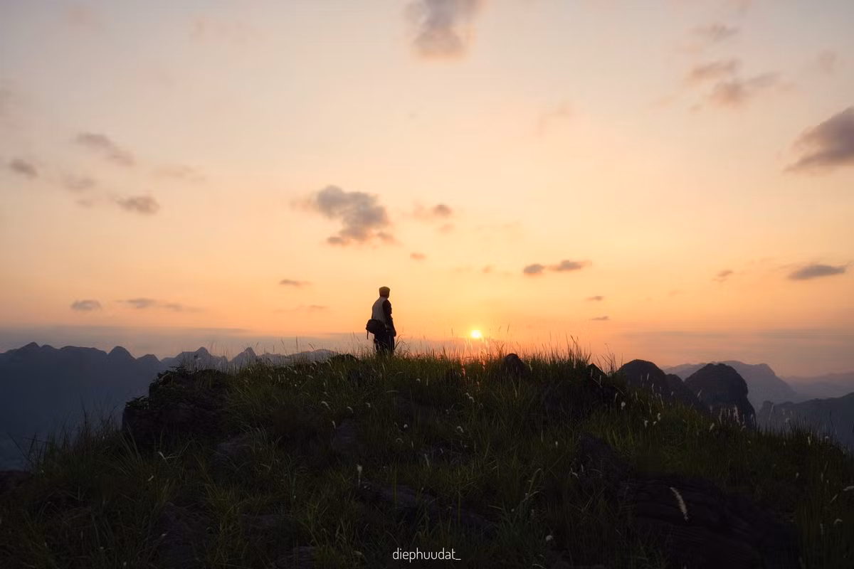 Từ trên cao nhìn xuống, sông Nho Quế hiện ra như một dải lụa xanh ngọc, uốn lượn giữa lòng núi đá. Khi mặt trời lặn dần, mặt nước phản chiếu sắc vàng cam rực rỡ, những tia nắng cuối cùng như níu giữ từng đường cong của sông, từng vách đá sừng sững. Cảnh vật lúc này như chậm lại, lắng đọng cùng bước chân người lữ khách. Ảnh Diệp Hữu Đạt