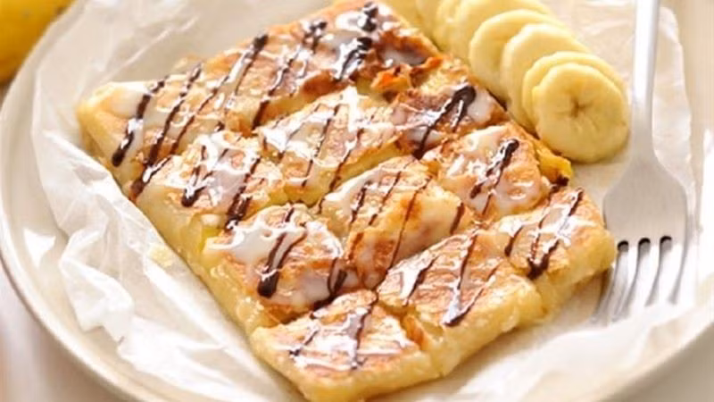 Bánh Roti nhân chuối (roti gluay) là món ăn vặt đường phố nổi tiếng Thái Lan với lớp vỏ bánh bột giòn tan thơm mùi bơ và sữa, cắn vào bên trong nhân chuối thơm ngon hòa quyện cùng vị béo thơm của trứng, chấm cùng một ít sữa đặc và socola. Món ăn này sẽ cực kỳ hợp với những tín đồ hảo ngọt. Ảnh Bachhoaxanh