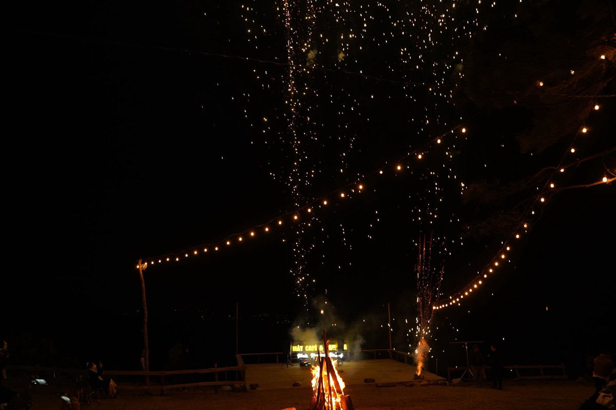 Buổi tối trên đỉnh núi trở nên ấm áp hơn với ánh lửa trại bập bùng, những dây đèn vàng treo giữa không gian tối, tiếng nhạc nhẹ vang lên giữa núi rừng.