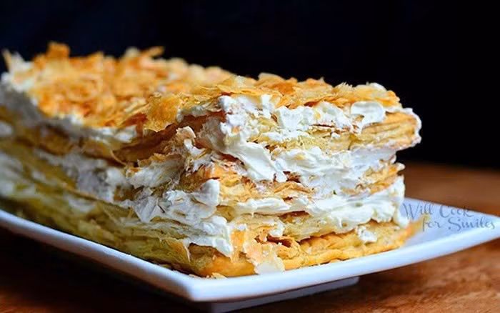 Bánh Napoleon, hay còn gọi là Mille-feuille (nghìn lớp lá), có xuất xứ từ vùng Naples, Ý. Điểm đặc trưng của loại bánh này là cấu trúc nhiều lớp độc đáo: lớp vỏ bột ngàn lớp (puff pastry) được cán mỏng tuyệt đối, khi nướng phồng lên, tạo thành những tầng giòn tan, vụn rụm và phát ra tiếng giòn rôm rốp đặc trưng. Đây cũng chính là yếu tố khiến Napoleon khác biệt hoàn toàn so với các loại bánh kem bông xốp thông thường. Ảnh Will Cook for Swiles