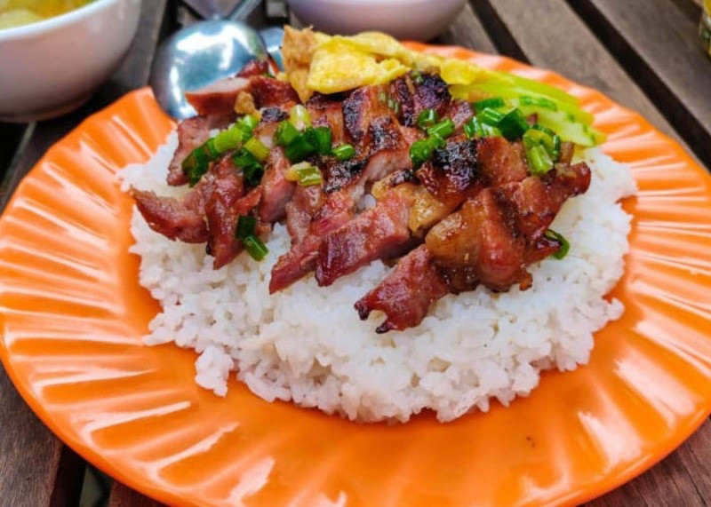 Buổi sáng ở Phnom Penh thường bắt đầu bằng mùi thịt heo nướng lan tỏa từ những bếp than ven đường. Bai sach chrouk – món cơm thịt heo nướng quen thuộc – xuất hiện khắp các góc phố với thịt heo thái mỏng, ướp gia vị nhẹ, hong khô rồi nướng đến khi xém cạnh. Thịt mềm, thơm, ăn cùng cơm trắng, đồ chua và nước sốt ớt ngọt, tạo nên bữa sáng giản dị nhưng tròn vị. Ảnh BHX