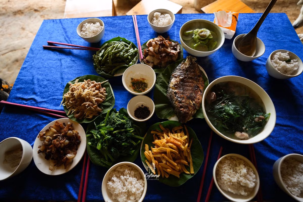 Ẩm thực tại bản Liền là một điểm cộng lớn. Các bữa ăn được phục vụ ngay tại homestay với nguyên liệu sạch từ vườn nhà hoặc hái trên rừng. Mỗi suất ăn khoảng 100.000 – 120.000 đồng, gồm các món đặc sản như gà đồi nướng, cá suối chiên giòn, rau rừng luộc chấm muối lạc, cơm lam, măng muối, thịt trâu gác bếp… Một số nhà còn mời khách tham gia nấu ăn cùng gia đình, từ việc hái rau, nhóm bếp củi đến bày biện mâm cơm – trải nghiệm khiến nhiều người lần đầu "về bản" cảm thấy bồi hồi, thích thú. Ảnh Hùng Vĩ