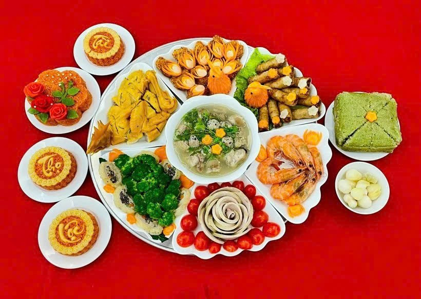 Mâm cỗ gồm gà luộc, tôm hấp xếp hoa, chả lụa tạo hình, thịt đông, xôi gấc, bánh chưng, nem rán, canh nóng và các món xào, nộm.