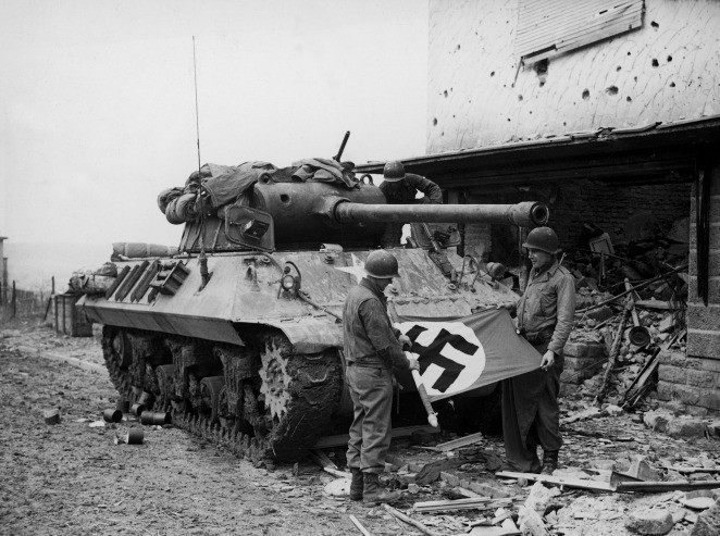 Hai lính Mỹ quấn cờ chữ thập ngoặc chết chóc của Hitler khi đứng trước xe tăng Sherman ở Bitburg tháng 2/1945.