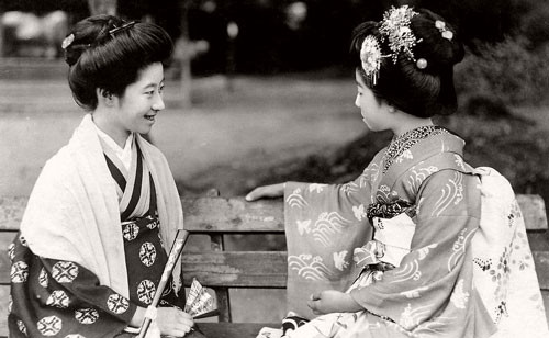 ##sc### Hai cô gái trẻ ngồi trên ghế đá công viên.