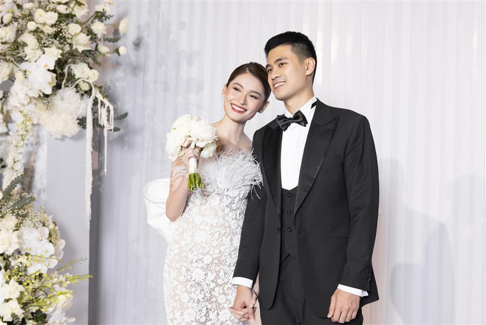 hùy Dung xuất hiện đón khách với chiếc váy ren trắng tinh tế. Trong khi đó, ông xã doanh nhân bảnh bao, lịch lãm với vest đen.