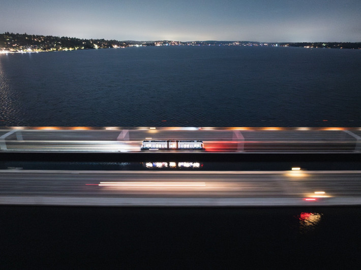 Trong loạt ảnh do Sound Transit công bố hôm thứ Tư, đường chân trời Bellevue, Washington, rực sáng từ xa khi đoàn tàu băng qua giữa làn đường hướng đông và hướng tây trên hồ. Góc nhìn của người soát vé cũng được hé lộ từ bên trong tàu.