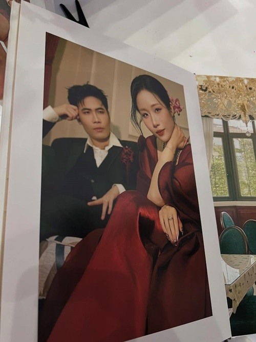 Chú rể diện vest tối màu dáng cổ điển, phong thái điềm đạm, ánh nhìn nghiêng về cô dâu đầy dịu dàng. Vợ Phúc Du gây ấn tượng với chiếc váy đỏ, chất liệu mềm rủ, thiết kế kín đáo nhưng sang trọng, kết hợp cùng kiểu tóc gọn gàng và phụ kiện hoa cài nhẹ nhàng, tạo cảm giác vừa nền nã vừa cuốn hút. Ảnh: Fanpage Thế Giới Showbiz.