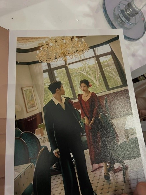 Một bức ảnh cưới mang không khí hoài niệm, ấm áp của Phúc Du được chụp trong không gian nội thất cổ điển với ánh đèn chùm vàng ấm làm điểm nhấn. Cặp đôi đứng cạnh nhau trong một khoảnh khắc tự nhiên, không tạo dáng cầu kỳ nhưng toát lên sự gắn bó và thân mật. Ảnh: Fanpage Thế Giới Showbiz.