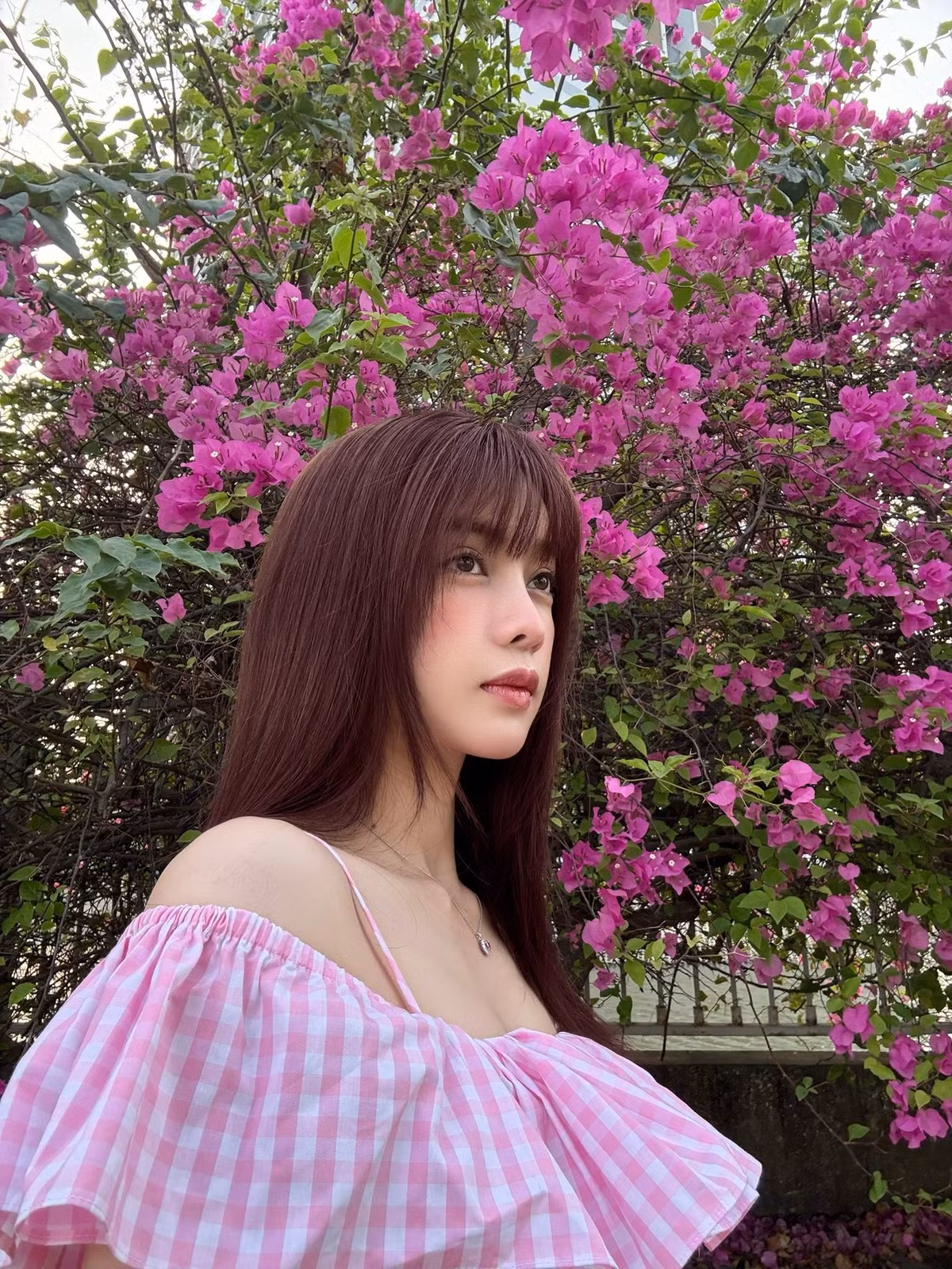 Chụp ảnh bên hoa, Trình Mỹ Duyên lựa chọn chiếc váy trễ vai họa tiết caro hồng – trắng, tôn lên bờ vai thon và xương quai xanh thanh mảnh.