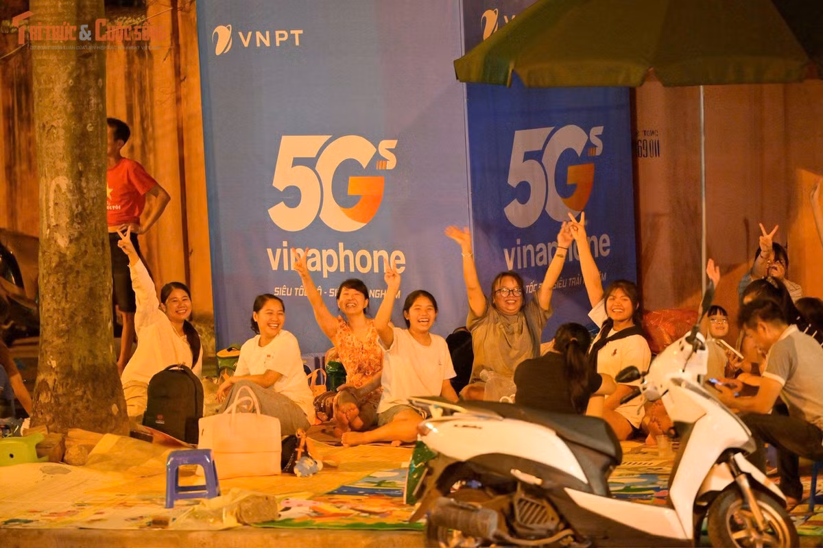 Trong ánh đèn phố, từng nhóm gia đình, bạn trẻ trải bạt, mang theo ghế nhựa, đồ ăn nhẹ, kiên nhẫn ngồi chờ xem diễu binh, diễu hành.