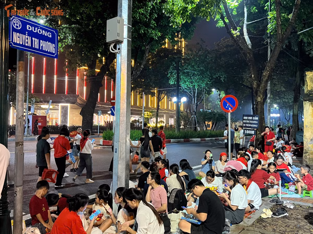 Trên vỉa hè, nhiều gia đình mang theo ghế nhựa nhỏ, chai nước, thậm chí cả đồ ăn vặt để tiện ngồi chờ. Một số bạn trẻ tranh thủ “xí chỗ” từ sớm, vừa ngồi vừa lướt điện thoại, trò chuyện, tạo trò chơi.