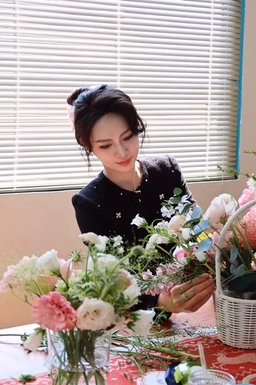 Rời ánh đèn sự kiện, Vũ Thúy Quỳnh trong khung cảnh cắm hoa mang diện mạo khác hẳn. Cô trang điểm nhẹ, biểu cảm tập trung. Không còn sắc đỏ nổi bật, cô chọn tông màu trầm, kín đáo nhưng vẫn thanh lịch.