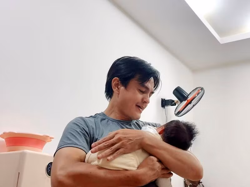 Ở những khoảnh khắc đời thường, Cao Minh Đạt không giấu được vẻ lúng túng nhưng đầy âu yếm khi bế con trong tay.