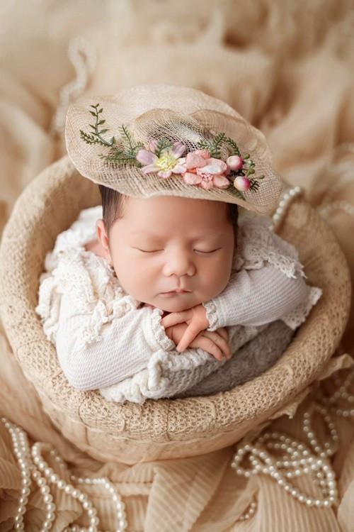 Trong concept chụp tại studio, cô nhóc say giấc trong chiếc giỏ mây nhỏ xinh, diện trang phục ren trắng, khi đội mũ hoa dịu dàng, lúc lại hóa thân thành “chú kỳ lân” đáng yêu.