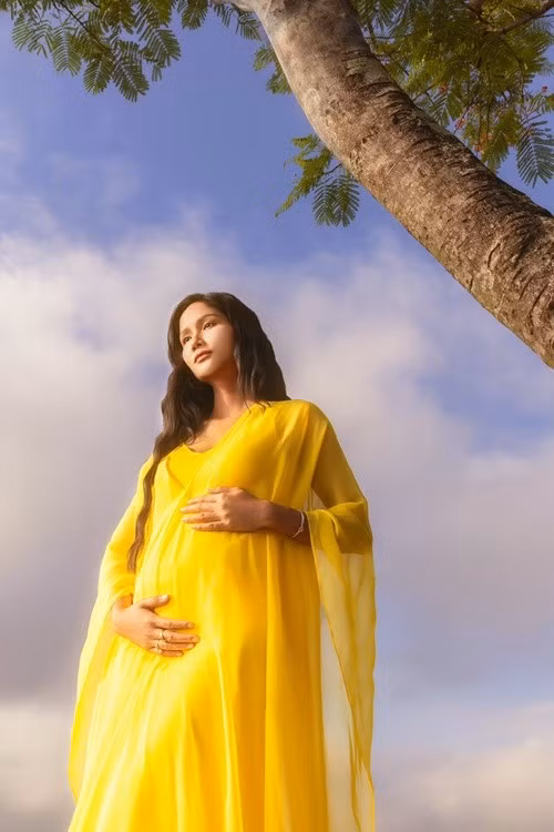 H'hen Niê mặc đầm vàng khoe bụng bầu. "Hen chọn chiếc đầm vàng cho khoảnh khắc đặc biệt này, bởi màu vàng luôn gắn với nhiều kỷ niệm của Hen, màu vàng của ánh sáng ngày mới, màu vàng của sự sinh sôi và rực rỡ", cô bày tỏ. Ảnh: FB H'hen Niê.