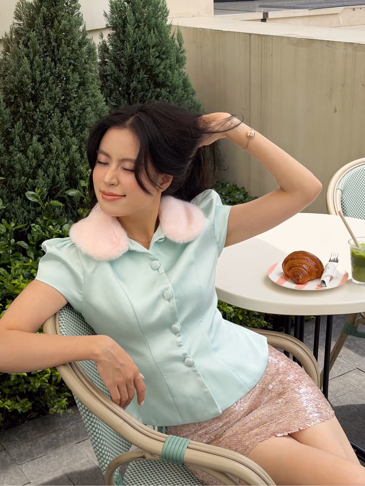 Hoàng Thùy Linh kết hợp áo xanh bạc hà viền lông hồng với chân váy sequin. Sự tương phản giữa chất liệu mềm và bề mặt bắt sáng giúp bộ đồ thu hút mà không cần nhiều phụ kiện.