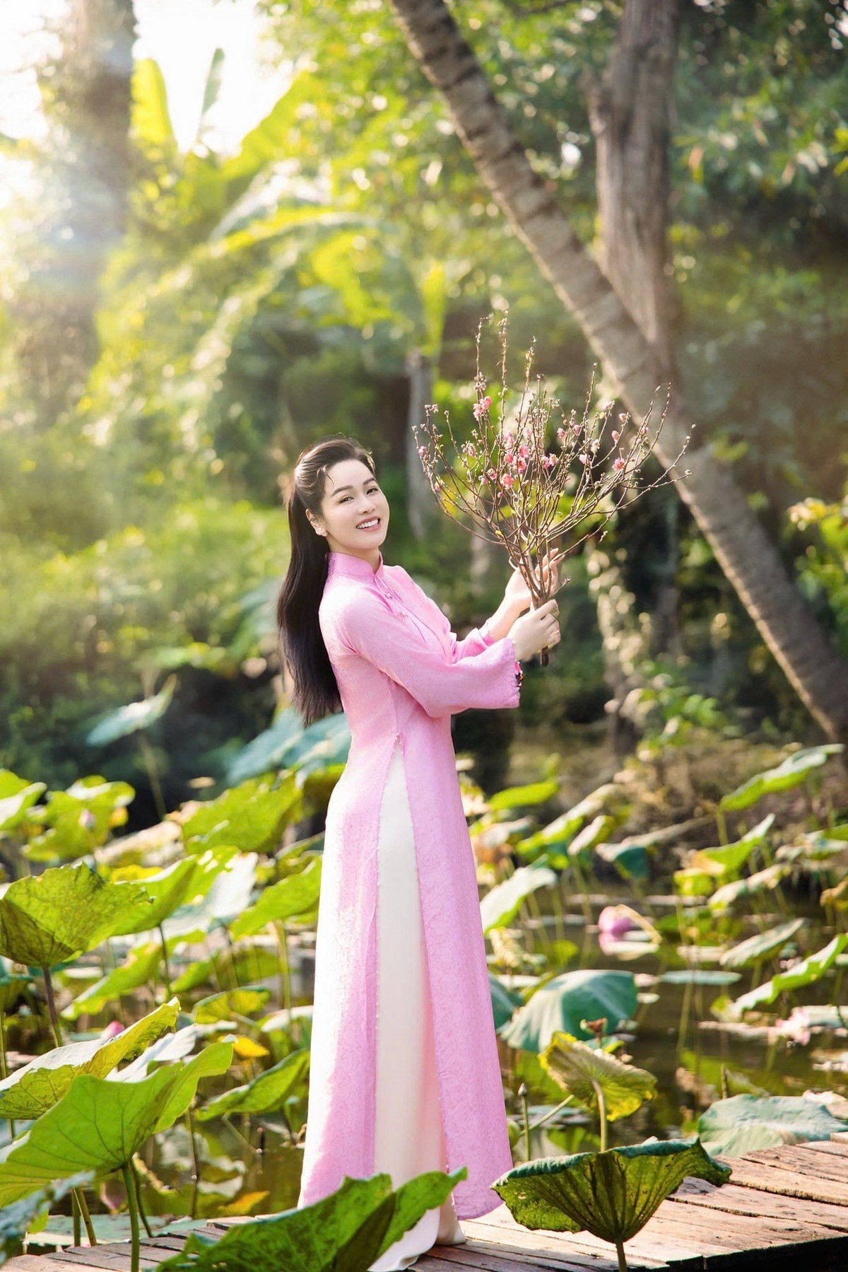 Nữ diễn viên – ca sĩ tạo dáng bên hồ sen, mai vàng và cành đào đỏ thắm để tăng sắc xuân cho bộ ảnh. Trên trang cá nhân, cô chia sẻ những câu thơ nhẹ nhàng, gửi gắm mong ước một năm mới an yên, nhiều niềm vui. “Áo hồng chạm nắng, xuân vừa kịp sang. Cười lên một cái, dịu dàng cả năm”, người đẹp viết trên trang cá nhân. Ảnh: FB Nhật Kim Anh.