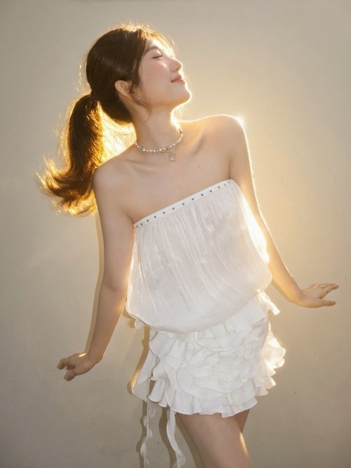 Cô diện bộ váy trắng hai tầng với phom dáng nhẹ nhàng. Kiểu tóc buộc thấp cùng phụ kiện tinh giản mang đến hình ảnh thanh thoát, nữ tính.