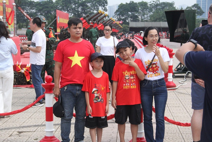 Một gia đình mặc áo với họa tiết lá cờ Tổ quốc tạo dáng chụp ảnh cùng dàn pháo lễ.