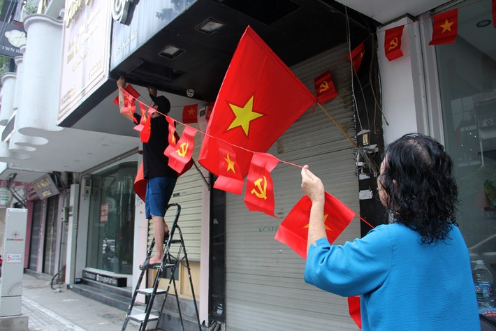 Bà chủ một cửa hàng kinh doanh trên phố Kim Mã cùng người thân tất bật hoàn thiện những hạng mục trang trí với nhiều lá cờ đỏ sao vàng, kèm theo lá cờ Đảng trong không khí hân hoan, rạng rỡ, niềm tự hào dân tộc và tình yêu quê hương, đất nước.