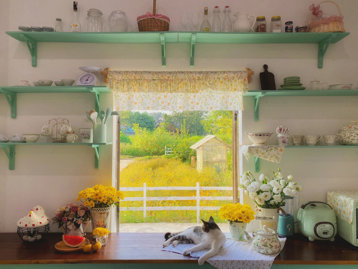 Chị Linh thừa nhận, quá trình cải tạo nhà khá vất vả. Chị tự lên ý tưởng thay vì thuê đơn vị thiết kế, tự học cách sơn tường, may rèm hay trang trí phòng. Mẹ và em trai cũng lên Mộc Châu phụ giúp, đóng cửa gỗ, bàn bếp và dựng hàng rào. (Góc bếp gọn gàng, xinh xắn với khung cửa sổ nhìn ra vườn hoa phía trước.)