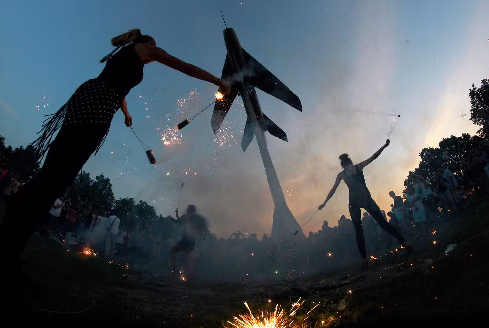 Các diễn viên đường phố biểu diễn dưới tượng đài tiêm kích MiG-19 làm phông nền phía sau.