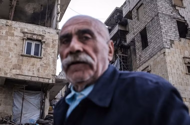 Người đàn ông lớn tuổi Syria đi ngang qua các tòa nhà đổ nát.
