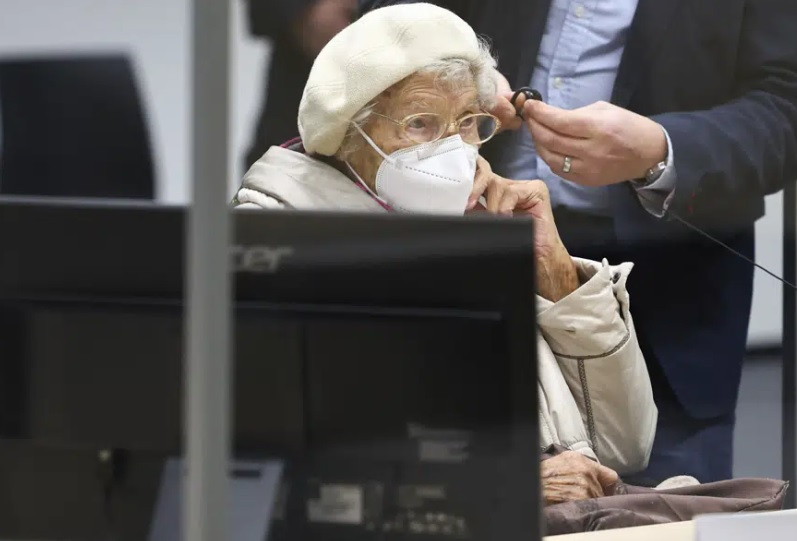 Tại phiên tòa, bà Irmgard ngồi trên xe lăn, đội mũ trắng, đeo khẩu trang y tế và có một chiếc chăn trên đùi.