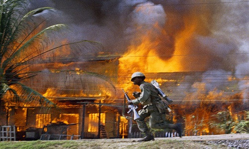Lính Mỹ di chuyển nhanh Mỹ qua những ngôi nhà mái lá đang bốc cháy dữ dội ở Sài Gòn tháng 6/1968.