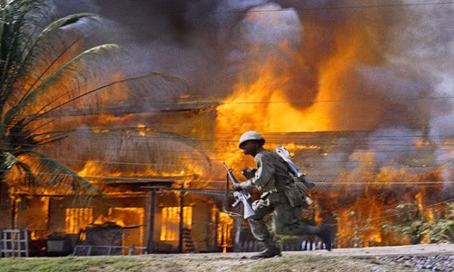 Lính Mỹ di chuyển nhanh Mỹ qua những ngôi nhà mái lá đang bốc cháy dữ dội ở Sài Gòn tháng 6/1968.