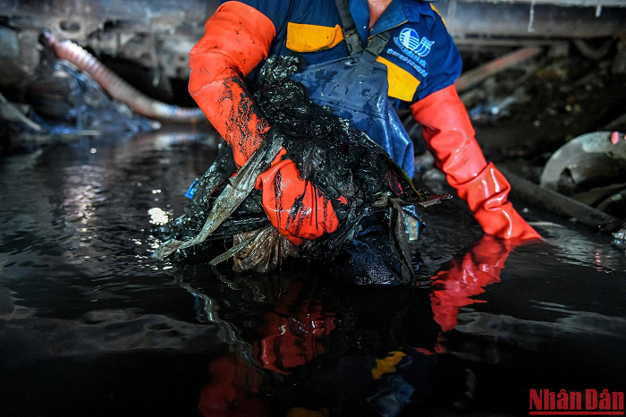 Người thợ cống già Đỗ Văn Công ôm theo rác để đưa ra ngoài. Sau nửa ca làm, nước cống đã tràn cả vào bên trong bộ đồ bảo hộ, hòa quyện với mồ hôi đã ướt đầm... 