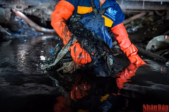 Người thợ cống già Đỗ Văn Công ôm theo rác để đưa ra ngoài. Sau nửa ca làm, nước cống đã tràn cả vào bên trong bộ đồ bảo hộ, hòa quyện với mồ hôi đã ướt đầm... 