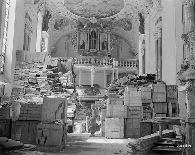 Từ năm 1943 - 1945, hơn 300 người đến từ 13 quốc gia tham gia chương trình Di tích, Mỹ thuật và Lưu trữ (MFAA) đã tìm kiếm những "kho báu" nghệ thuật bị lính Đức quốc xã cướp bóc rồi đem cất giấu ở nhiều nơi. Trong ảnh là một binh lính Mỹ kiểm tra một "kho báu" nghệ thuật được Đức quốc xã giấu trong một nhà thờ ở Elligen.