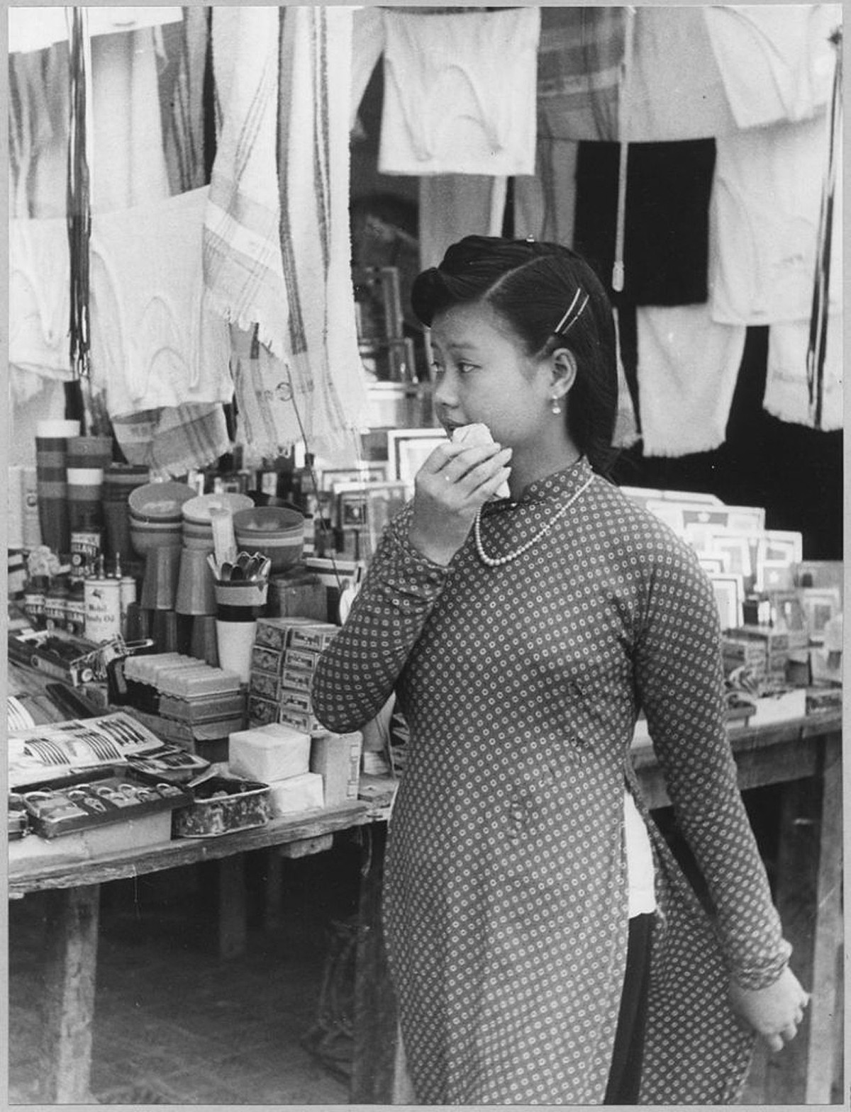 Thiếu nữ Hà Nội mặc áo dài đứng trước một quầy hàng.