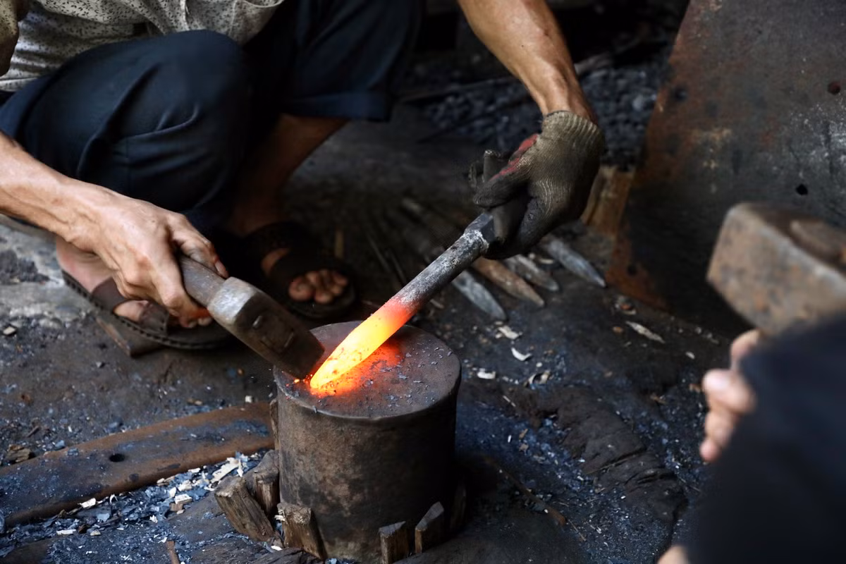 "Để tạo ra được một sản phẩm có chất lượng tốt, phải trải qua rất nhiều công đoạn. Khâu quan trọng và đòi hỏi nhiều kỹ thuật nhất là tôi thép và làm nguội. Đầu tiên, sẽ cắt các bản sắt thành hình dạng của sản phẩm, sau đó cho lên lò nung với nhiệt độ hơn 1.000 độ C. Thời gian nung sẽ tùy vào từng loại nguyên liệu thép và sản phẩm tạo ra dày, mỏng. Khi phôi thép nung chuyển sang màu đỏ trắng là lúc đặt lên đe để quai búa", ông Cung chia sẻ. Ảnh: Rèn mũi khoan bê tông.