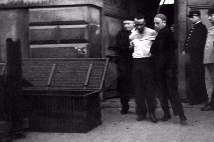 Nhân viên công vụ dẫn giải Weidmann đến bên máy chém, đi qua một cái hòm dùng để vận chuyển thi thể của y sau đó.