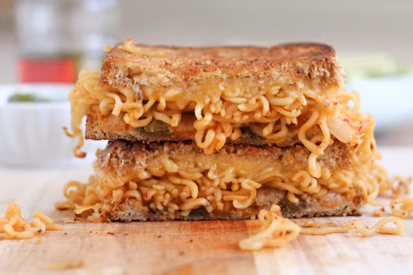 Tiếp tục rưới tương ớt, xếp phô mai, thịt xông khói lên một mặt miếng mì trong chảo và đậy vung lại. Đun nhỏ lửa tới khi phô mai tan chảy thì úp hai miếng mỳ chiên lại với nhau là có chiếc sandwich mỳ tôm cực kỳ ngon và độc đáo.