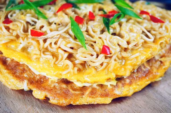 Để làm pizza mỳ tôm, người ta thái sợi phô mai, còn ớt và hành thái hạt lựu. Lấy 2 vắt mỳ tôm chần qua nước đun sôi. Bắc chảo lên bếp, đổ mỳ đã chần vào dàn đều mặt chảo cho mỳ xếp thành hình tròn.