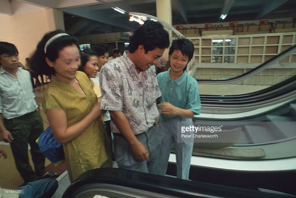 Khách mua sắm trải nghiệm chiếc thang cuốn đầu tiên ở Việt Nam tại chợ An Đông mới, Sài Gòn năm 1992. Có cả một nhân viên túc trực tại thang để giúp đỡ du khách.