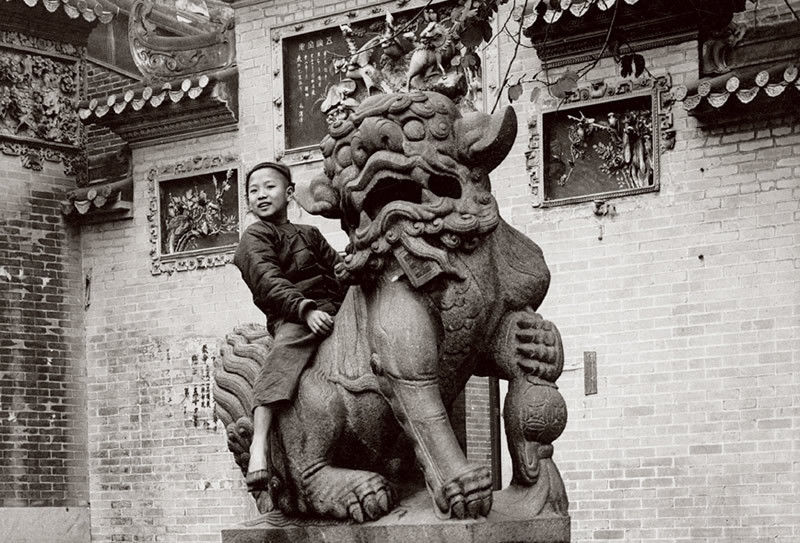 Một cậu bé tinh nghịch cưỡi trên lưng sư tử đá.