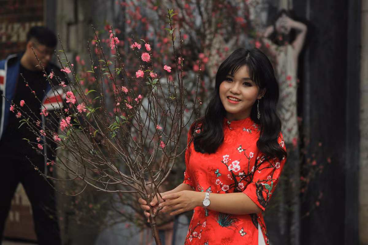 Tay cầm cành đào hồng, cô gái duyên dáng bên tà áo dài thướt tha trước ống kính để lưu lại những kỷ niệm đẹp khi Tết đến Xuân về.