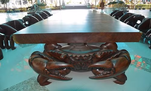 Hai đầu bàn là hai chú cua khổng lồ giơ càng với tư thế rất mạnh mẽ đang đỡ chiếc bàn trên mai của mình, hỗ trợ thêm cho hai chú cua này là hai chiếc ghế nhỏ đặt ở giữa bán phía dưới; còn 11 chiếc ghế cũng là những chú cua được tạo từ gỗ gõ đỏ nguyên khối, riêng chú cua đầu bàn, gọi là chú cua đầu đàn, được làm bằng gỗ lim.