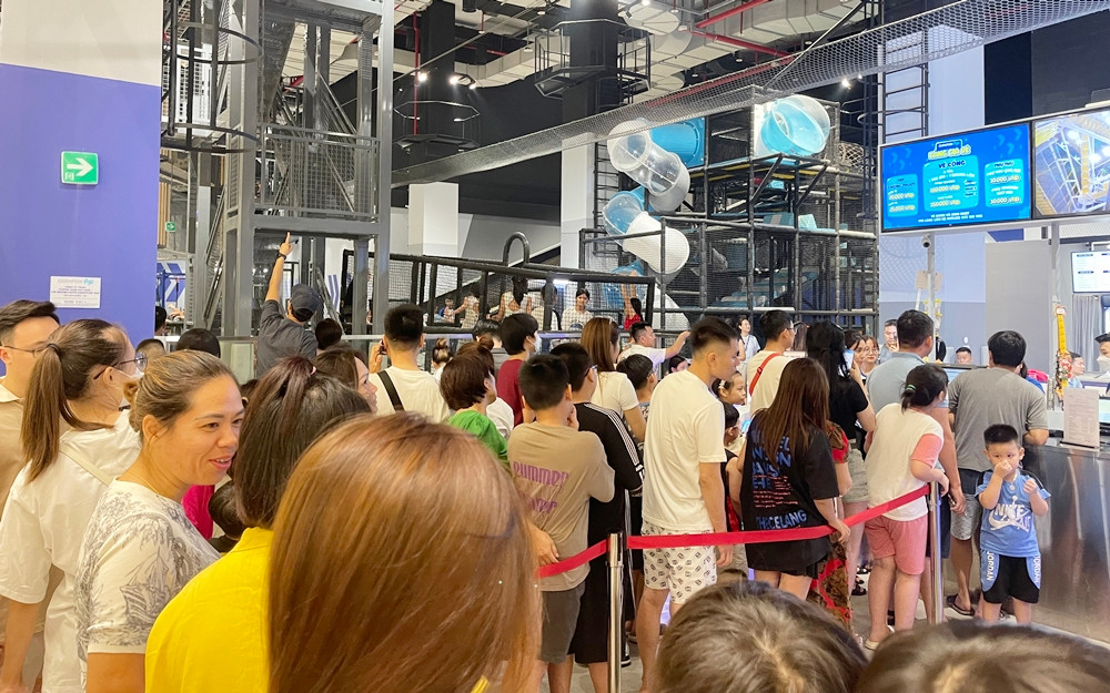 Nhiều phụ huynh và trẻ nhỏ đứng xếp hàng tại khu vực vui chơi dành cho trẻ nhỏ trong TTTM.