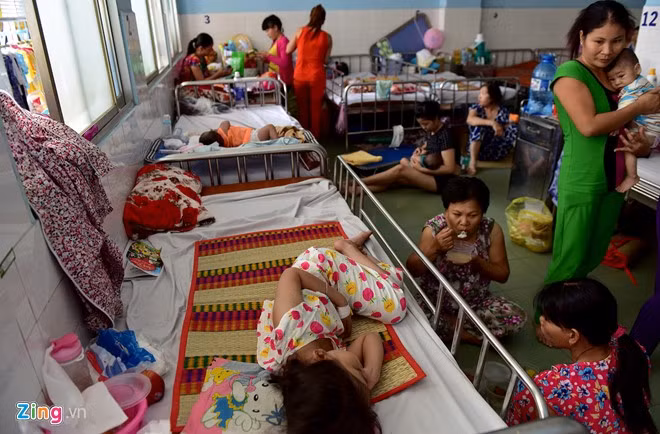 Bên trong các phòng điều trị cũng kín chỗ. Trẻ em nằm, người lớn đứng ngồi xung quanh để chăm sóc.