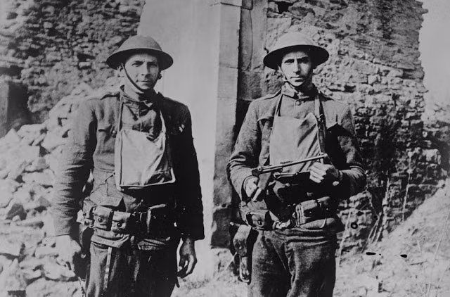 Hai lính Mỹ đứng trước một tòa nhà bị phá hủy nghiêm trọng bởi bom đạn chiến tranh.