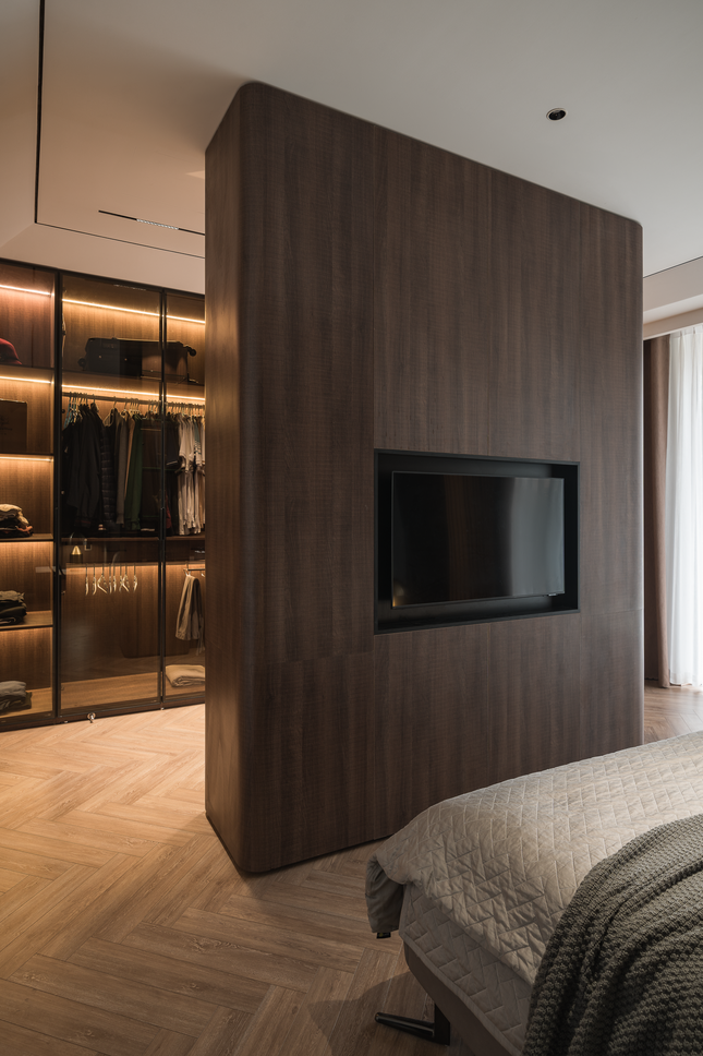 Khu vực ngủ và thay đồ được tách lớp không gian bằng một hệ tủ hai mặt. Mặt trong của tủ được sử dụng như khu trang điểm và trưng bày túi xách, trong khi mặt ngoài được thiết kế với hệ vách ngăn và tivi, giúp tối ưu hóa không gian sống. Luồng giao thông được thiết kế rất thuận tiện, giúp gia chủ dễ dàng di chuyển giữa các khu vực một cách tiện lợi.