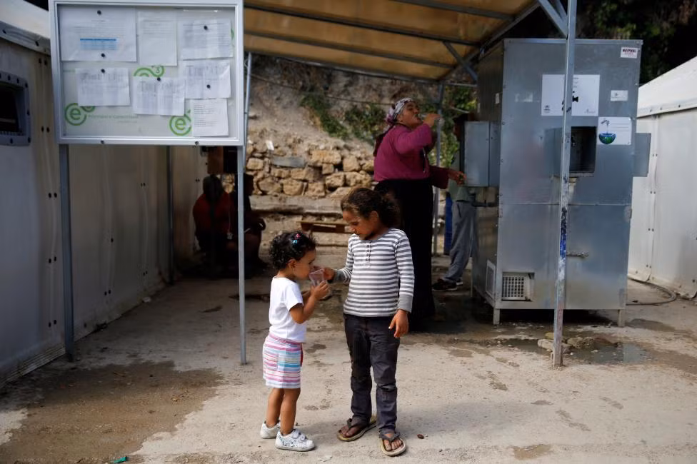 Một bé gái Syria đang cho em uống nước tại khu trại tị nạn Souda.