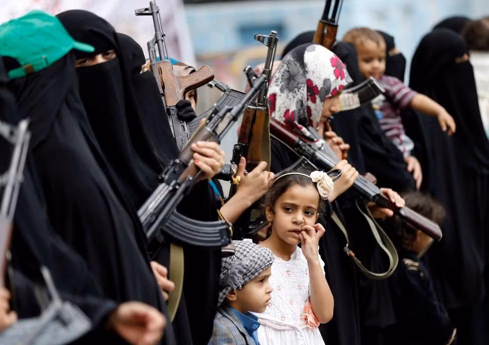 Các em nhỏ đứng nhìn đội nữ chiến binh trên đường phố Sanaa.
