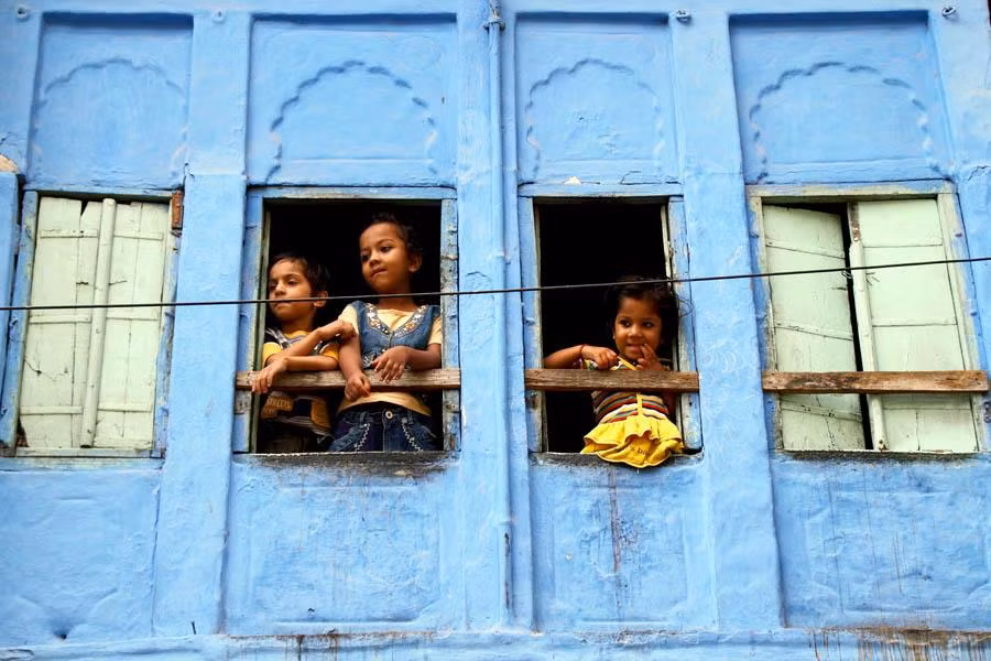 Những em nhỏ Ấn Độ nhìn xuống đường phố đông đúc từ ô cửa sổ.